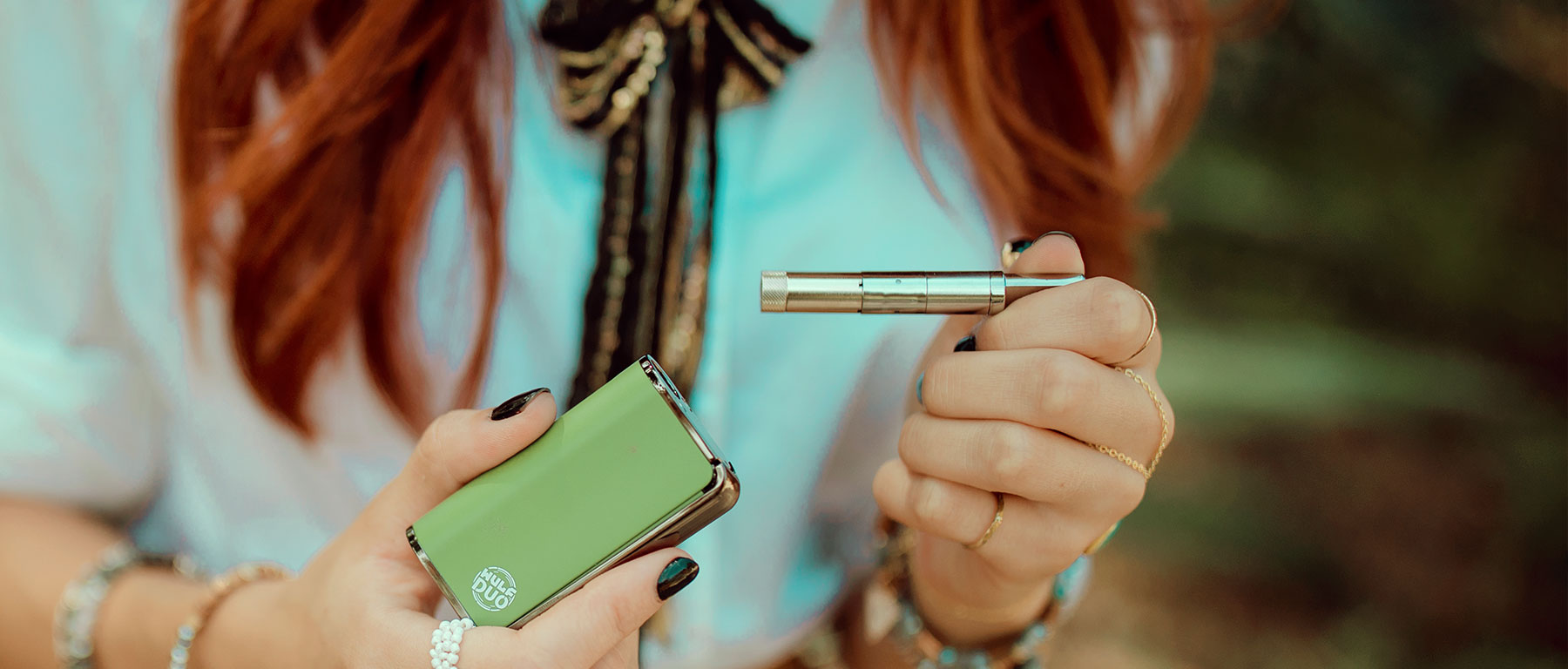 Woman with red hair and white shirt pulling vape tank out of Wulf Mods Duo outside at park
